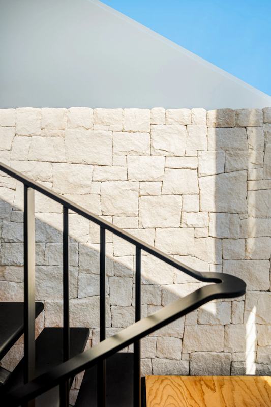 Split-face sandstone feature wall beside a black steel staircase